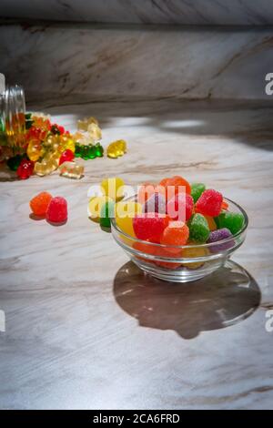 Granulated sugar coated candy gumdrops with spilled jar of gummy bears in background Stock Photo