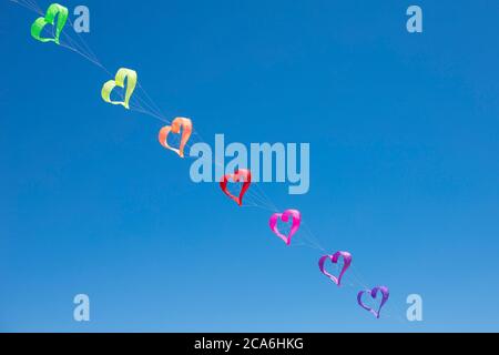 A row of rainbow coloured heart shaped kites flying in the blue sky. Background or wallpaper. Stock Photo