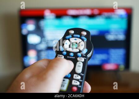 Hand using a TV remote control with the television out of focus Stock Photo
