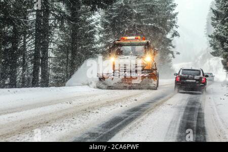 Liptovsky Hradok, Slovakia - January 08, 2019: Orange maintenance plough truck on forest road in snowstorm blizzard. Roads in this area get dangerous Stock Photo