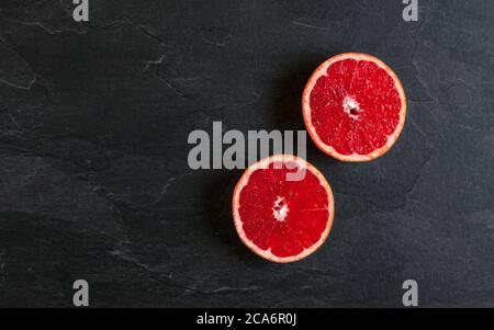 Flat lay photo - pink grapefruit cut in two halves, on black slate board Stock Photo
