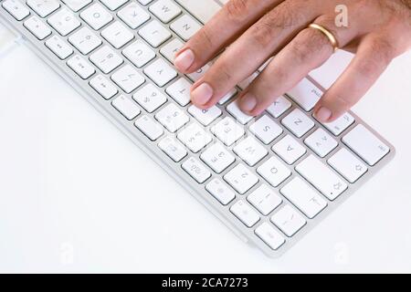 male hand typing on a white keyboard on a white table. White background. Stock Photo
