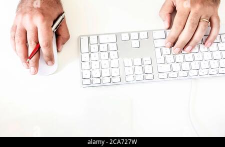a male while using the computer keyboard and mouse holding out a red pen in his right hand. Technology and creativity. Creative work Stock Photo