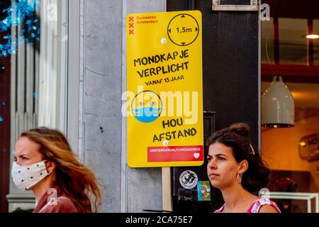 Women pass by a notice informing people about the mandatory wearing of masks and 1.5 meter distance on calf street. As of 5th August, wearing of face masks is going to be mandatory in busy places in Amsterdam such as malls, shopping streets, public transport and all public places following the recent concerns about a wide return of coronavirus in the Netherlands. Stock Photo