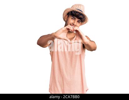Young hispanic man wearing summer hat smiling in love doing heart symbol shape with hands. romantic concept. Stock Photo