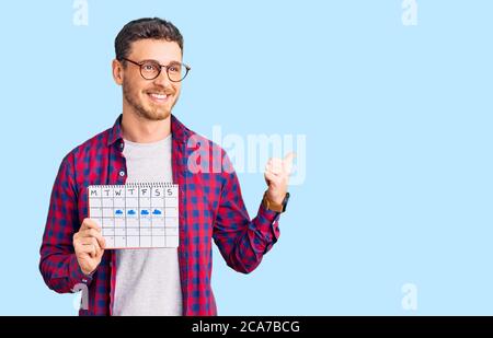 Handsome young man with bear holding travel calendar pointing thumb up to the side smiling happy with open mouth Stock Photo