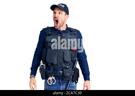 Young handsome man wearing police uniform angry and mad screaming frustrated and furious, shouting with anger. rage and aggressive concept. Stock Photo