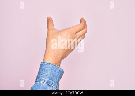 Hand of caucasian young man showing fingers over isolated pink background holding invisible object, empty hand doing clipping and grabbing gesture Stock Photo