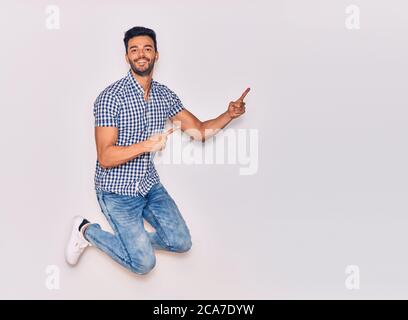 Young handsome hispanic man wearing casual clothes smiling happy. Jumping with smile on face pointing with fingers to the side over isolated white bac Stock Photo
