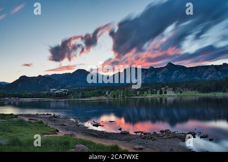 Long exposure sunset over lake estes. Fiery clouds roll over rocky mountains in the distance showing colorful reflection on the lake Stock Photo