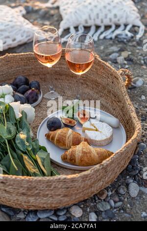 Vertical image of the outdoor picnic with wine, figs, croissants and camamber cheese in a woven basket. Stock Photo