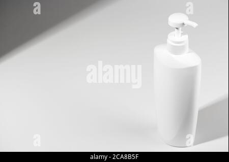 White unbranded bottle with dispenser on light shadow background. Blank container for lotion, cream, sunscreen, shampoo or hair conditioner. Mockup st Stock Photo