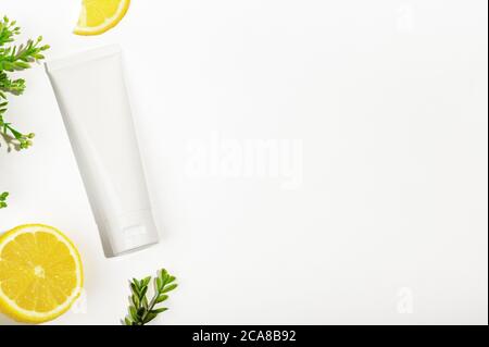 Top view of white unbranded tube with green plant and juicy lemon. Blank flacon for natural cosmetic products. Container for nutritious cream, body sc Stock Photo