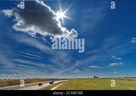 White traces of condensation of water vapor in the form of lines from aircraft flying over the highway. Cars are driving along the road at high speed Stock Photo