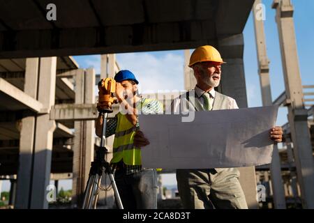 Two satisfied engineers talking at building site with construction structure in background Stock Photo