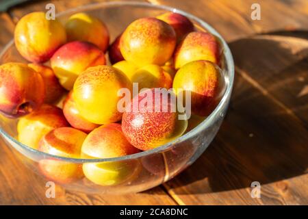 ripe juicy nectarines in a glass bowl on a wooden table on a sunny day Stock Photo