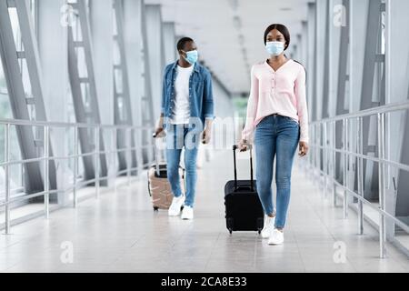 Pandemic Travels. Black People In Masks Walking With Luggage At Airport Terminal Stock Photo