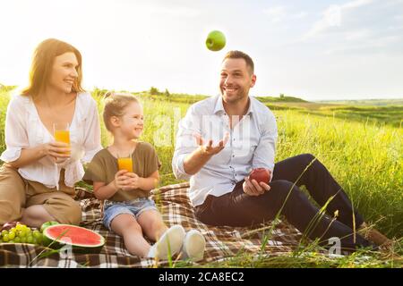 Happy dad juggling with apples on a picnic outside Stock Photo