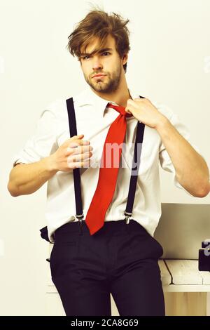 Bearded man, short beard. Caucasian stylish manager with moustache in red tie, shirt with suspenders sitting on table in studio on white background Stock Photo