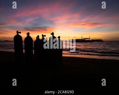 Sunrise over the beach in Philippines. Diving boats waiting for early morning divers. Silhouette of diving tanks in the foreground. Stock Photo