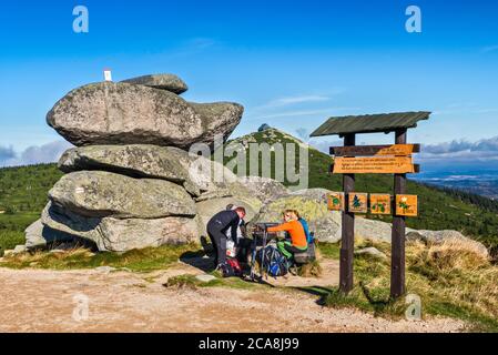 Hikers at picnic table at rock formation, international border post on top, in Karkonosze range, Karkonosze Natl Park, Lower Silesia, Poland Stock Photo