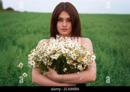 beautiful brunette girl with a bouquet of daisies flowers on a field with daisies Stock Photo