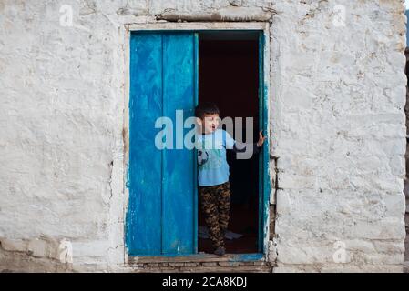 Xinaliq / Azerbaijan - July 8, 2019: portrait of boy next to blue door of house with white wall Stock Photo