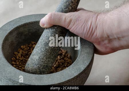 The hand of an adult Caucasian man grinds random medicinal roots and herbs in stone mortar. Mixture of dried medicinal herbs is ground by hand. Altern Stock Photo