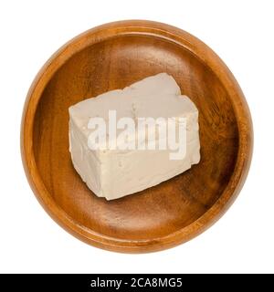 Fresh bakers yeast block in a wooden bowl. Compressed fresh yeast, used in baking as leavening agent to convert sugars in dough to carbon dioxide. Stock Photo