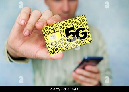 man holds a yellow SIM card with the inscription 5G and a mobile phone in his hand. Replacing the SIM card and switching to high-speed Internet. Stock Photo