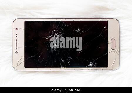 An old iPhone with a broken black screen on a white background. Stock Photo
