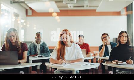 Male and female students sitting in classroom and making notes during the lecture. Students in high school classroom. Stock Photo