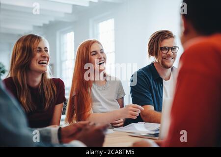 Cheerful male and female students sitting around a table in university. College classmates smiling during group study. Stock Photo