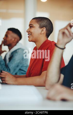 Smiling female student sitting in college classroom. Girl attending a lecture in university classroom. Stock Photo