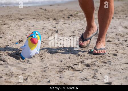 two inflatable toy pelicans, on the sand of the beach. Alongside particular of a person walking in slippers Stock Photo