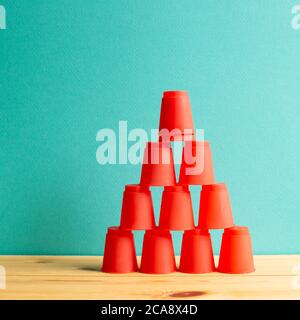 Pyramid of red plastic cups on wooden table with green background Stock Photo