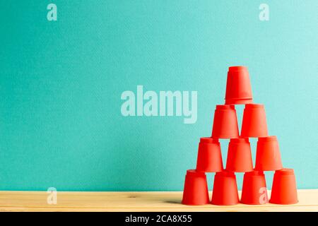 Pyramid of red plastic cups on wooden table with green background Stock Photo