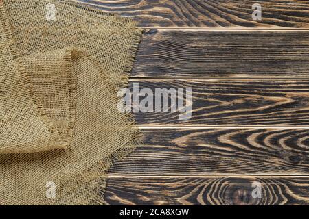 Copy space on a rustic textured wood tabletop painted with black paint and burlap of natural color on the side. Empty surface of textured wood planks Stock Photo
