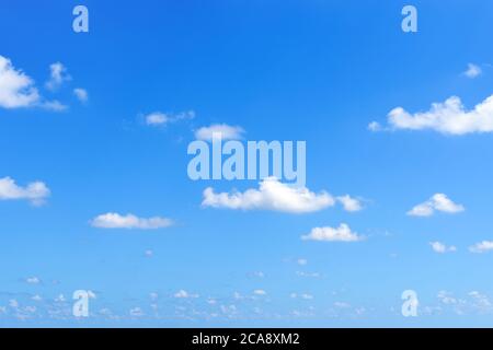 Sparse small white fluffy clouds float slowly high in the bright blue summer sky on a sunny day. Concept of good weather, summer holidays, vacations. Stock Photo