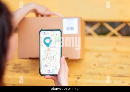 A woman scans the parcel code using her smartphone. Online map on the cellphone. Concept of courier delivery and modern technologies. Stock Photo