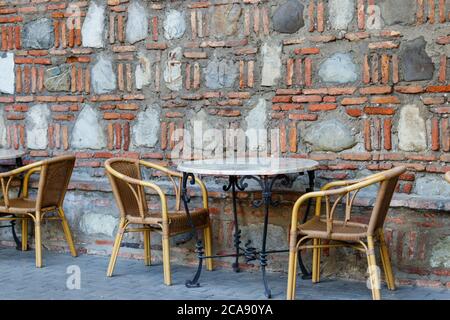 Tables and chairs in outdoor cafe. Patio set against stone wall Stock Photo