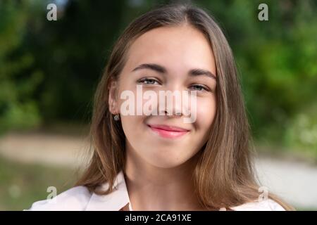 Beautiful smiling teenage girl in blue blouse, against green of summer park. Stock Photo