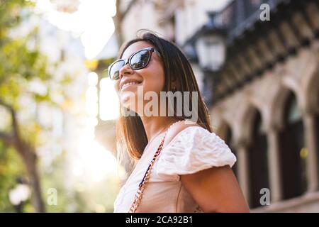 woman with sunglasses smiles as she walks through town Stock Photo