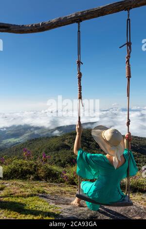 A young woman using a swing over a view of rainforest-covered mountains in the Ibitipoca Reserve, Minas Gerais, Brazil, South America Stock Photo