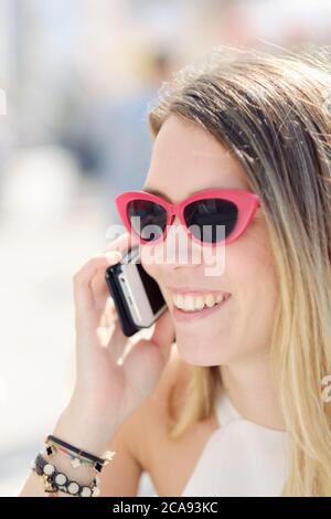 Headshot of a smiling young woman in sunglasses using her mobile phone outdoors, Portugal, Europe Stock Photo