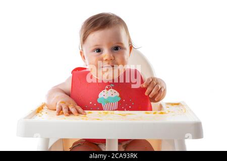 Cheerful baby child eats food itself with hands. Portrait of happy dirty kid boy in high chair and messy  around. Stock Photo