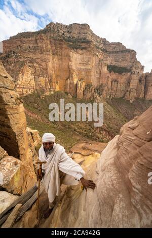 Ethiopian priest leaning on steep rocks leading to Abuna Yemata Guh church, Gheralta Mountains, Tigray Region, Ethiopia, Africa Stock Photo