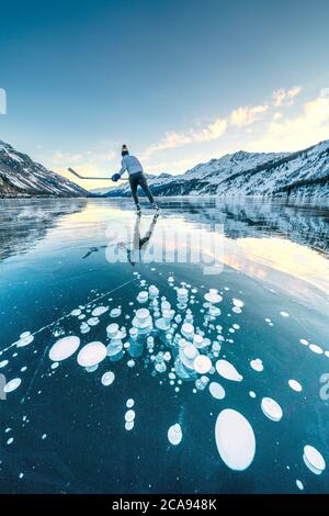 Ice hockey player skating on frozen Lake Sils covered of bubbles, Engadine, canton of Graubunden, Switzerland, Europe Stock Photo