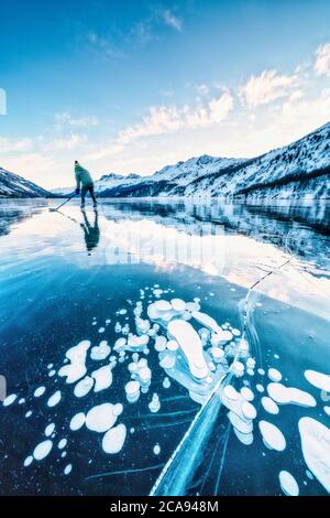 Man playing ice hockey on frozen Lake Sils covered of bubbles, Engadine, canton of Graubunden, Switzerland, Europe Stock Photo