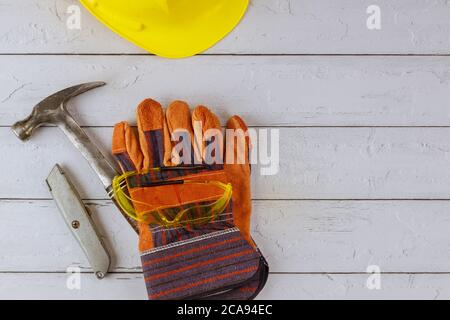 Construction work leather glove hand in construction safety helmet safety glasses construction hammer on a wooden white background Stock Photo